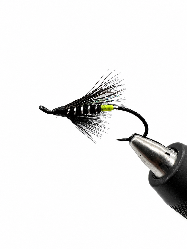 Black fishing lure with green butt and barbed tail, on a hook