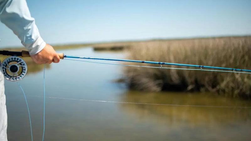 Load image into Gallery viewer, TFO Axiom II-X fishing rod held over water, blue blank and cork handle
