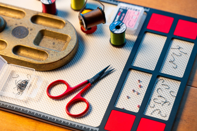 Load image into Gallery viewer, Fly tying mat with beige grid pockets and red compartments, hooks and scissors nearby
