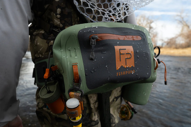 Load image into Gallery viewer, Close-up of olive green submersible lumbar pack with orange logo and front zipper panel
