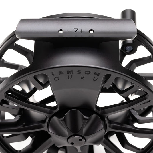 Black fly fishing reel with top bar and engraved center badge.