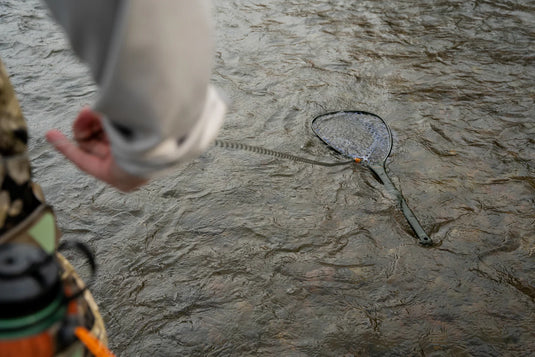 Fishing net release with thin line and orange latch on a rocky surface, held in hand