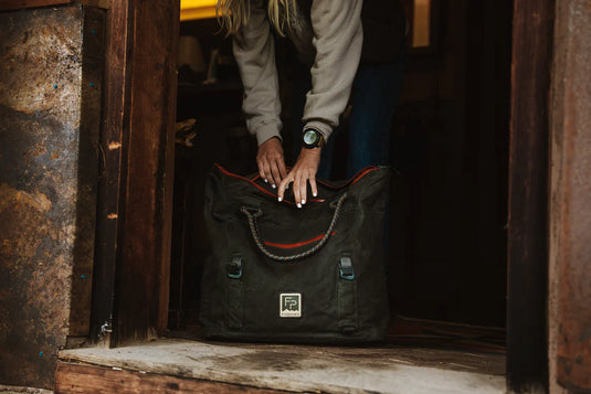 Dark green tote bag with orange-trim opening and front logo patch, close-up