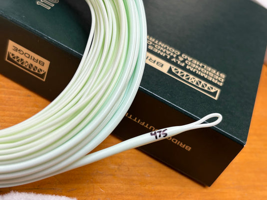 Coiled spey fly line in pale green and white beside dark Bridge boxes
