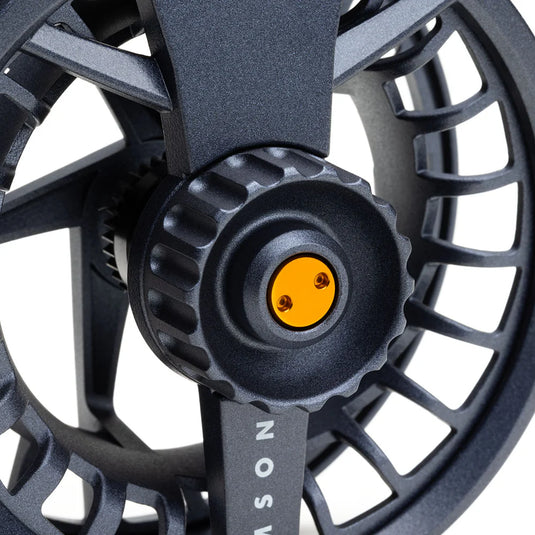 Fly fishing reel close-up: dark gray center cap with yellow insert and screw detail