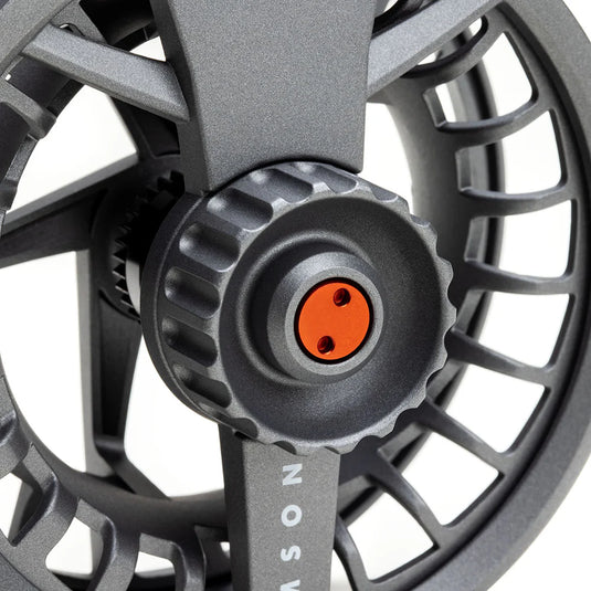 Fly fishing reel close-up: dark gray center cap with orange insert and screw detail