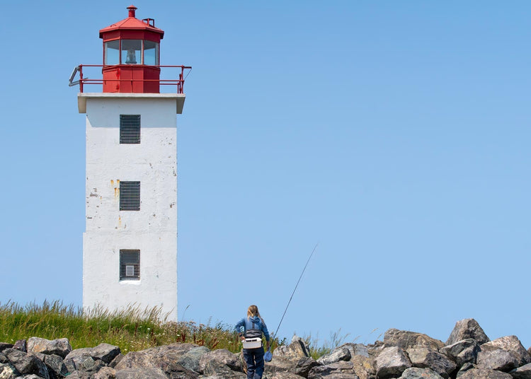 Red and white lighthouse on a rocky outcrop with a clear blue sky.