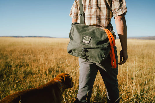 Back view of dark green fishing satchel worn on shoulder with flap closure