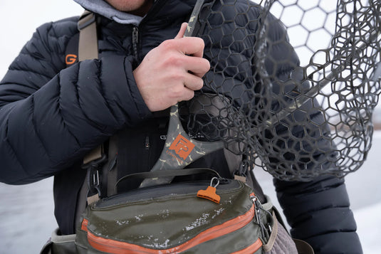 Fish landing net held beside a jacket, dark hex-pattern mesh and oval hoop