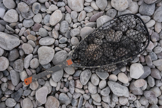 Fish landing net with black mesh and dark handle, lying on gray rocks