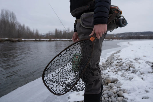 Landing net held outdoors, dark hex-mesh bag with brown handle