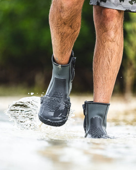 Dark gray zippered bootie with hex tread, worn on feet in shallow water