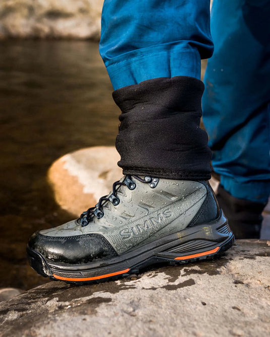 Rubber-sole boot on rocky ground, dark upper, lace-up front, orange trim.