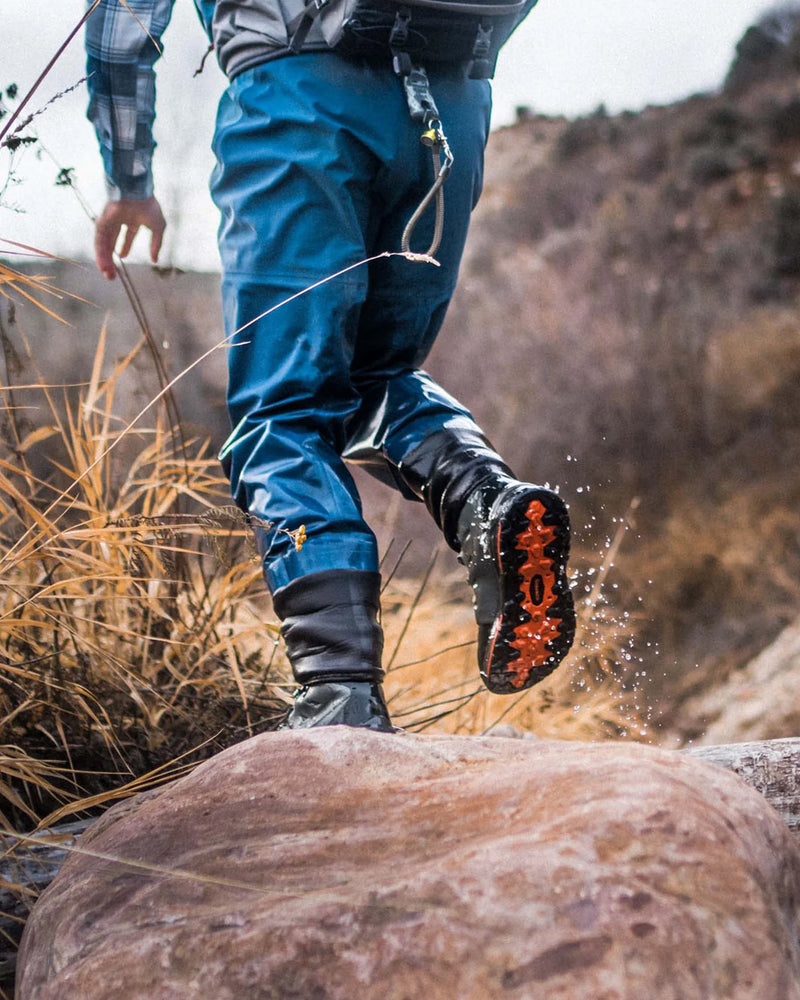 Load image into Gallery viewer, Lace-up rubber-sole boot stepping near rocks, dark upper with orange outsole.
