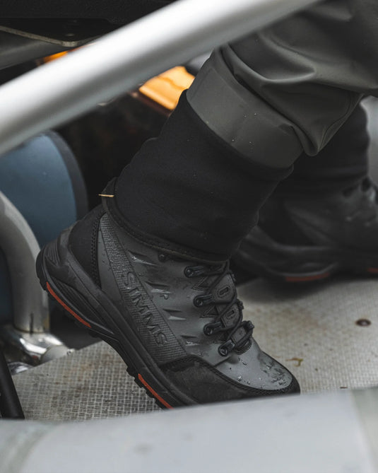 Rubber-sole boot close-up in car, gray lace-up upper, dark toe, orange stripe.