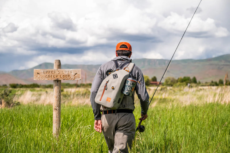 Load image into Gallery viewer, Submersible sling bag worn on a person, light gray with orange straps and front pocket
