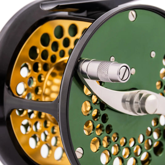 Green fishing reel with metal handle and perforated spool in gold behind it
