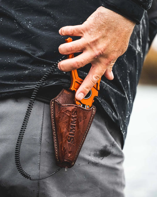 Hands placing orange guide pliers into a brown leather sheath on a jacket