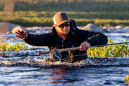 Dark hooded wading jacket with front zipper worn by an angler