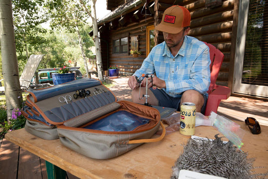 Fly tying kit case open on work table with tool pockets and vise area